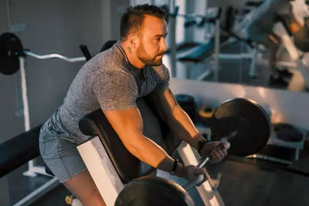 Man lifting barbell and doing preacher curls